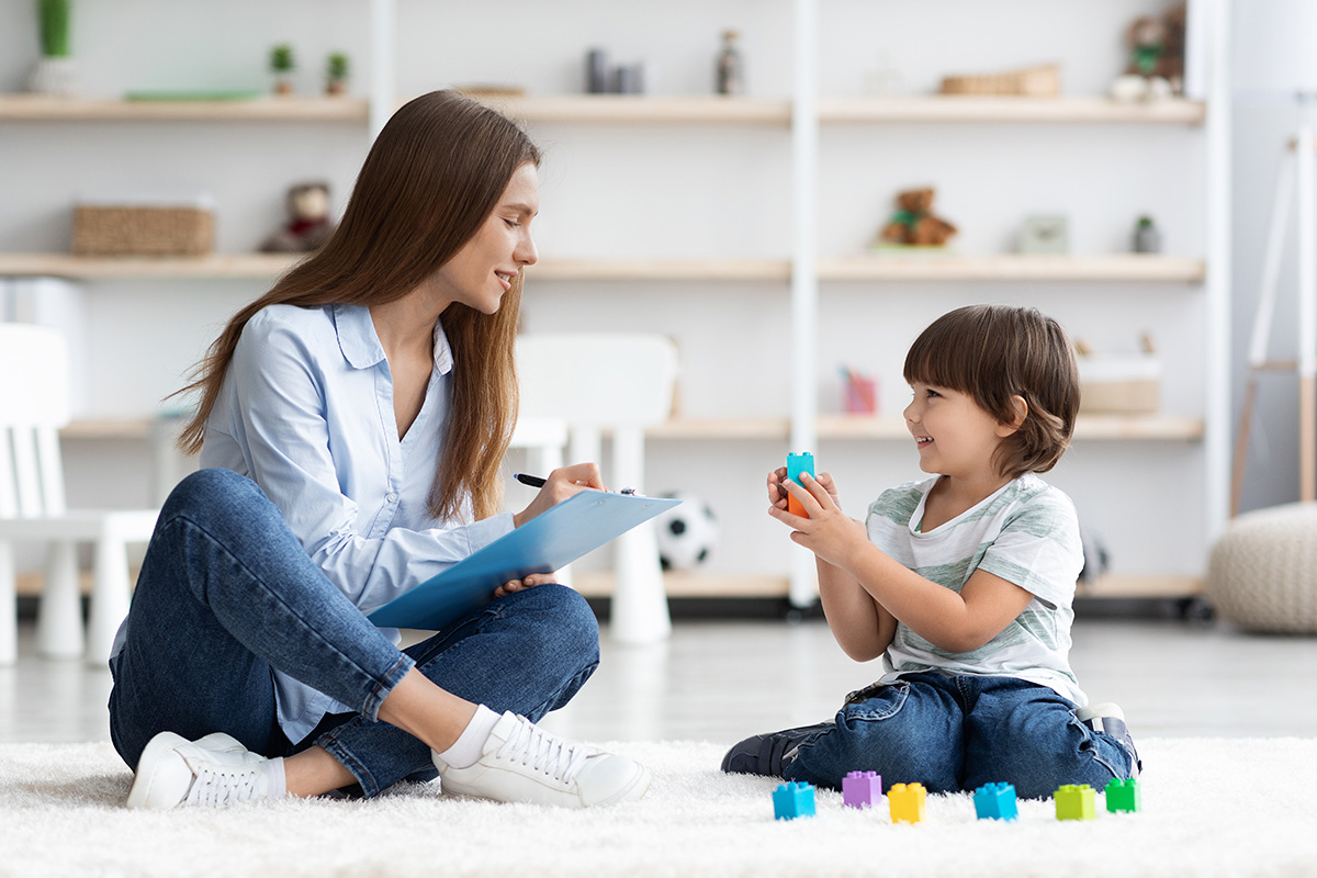 A woman sitting on the floor with a child, both looking at a tablet, while another person sits nearby holding a smartphone, all in a modern living room setting.