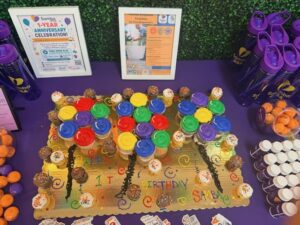 Rainbow cupcake cake reading "Happy 1st Birthday Samba" next to a framed 1-Year Anniversary Celebration sign